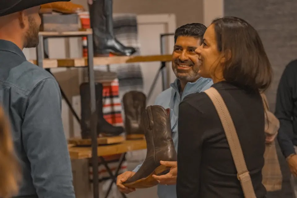 Guests smile as they look at a cowboy boot during a Chisos group fitting