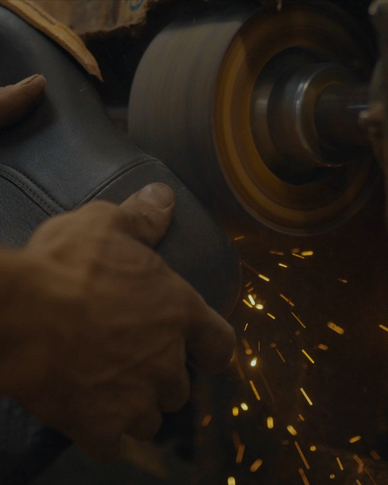 A bootmaker leveling the heel on a grinding wheel, throwing sparks